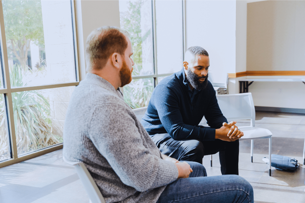 A focused one-on-one discussion in London, Kentucky Drug and Alcohol Rehab Resources. Two men sit and talk near large windows, highlighting the importance of personal support in recovery.