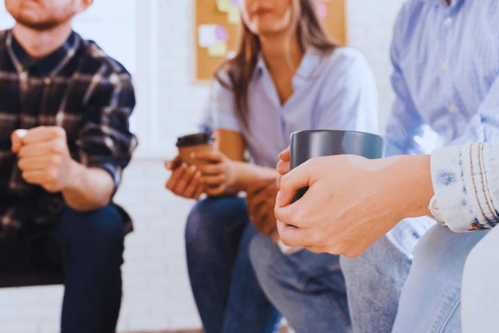 Participants holding coffee mugs while engaged in conversation during a group therapy session as part of Mount Sterling Kentucky Drug and Alcohol Rehab Resources.