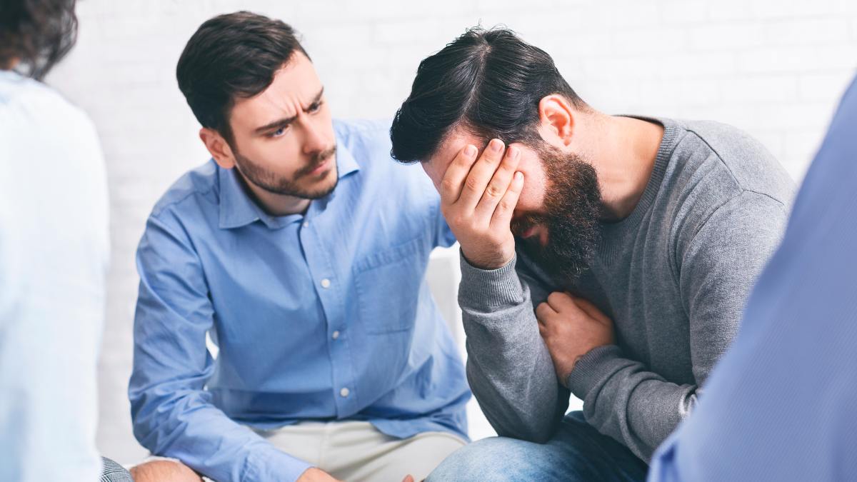 Man supporting a friend during group therapy to address addiction recovery questions and answers. 
