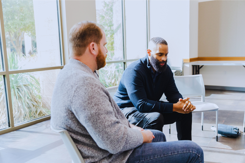 A focused one-on-one discussion in London, Kentucky Drug and Alcohol Rehab Resources. Two men sit and talk near large windows, highlighting the importance of personal support in recovery.
